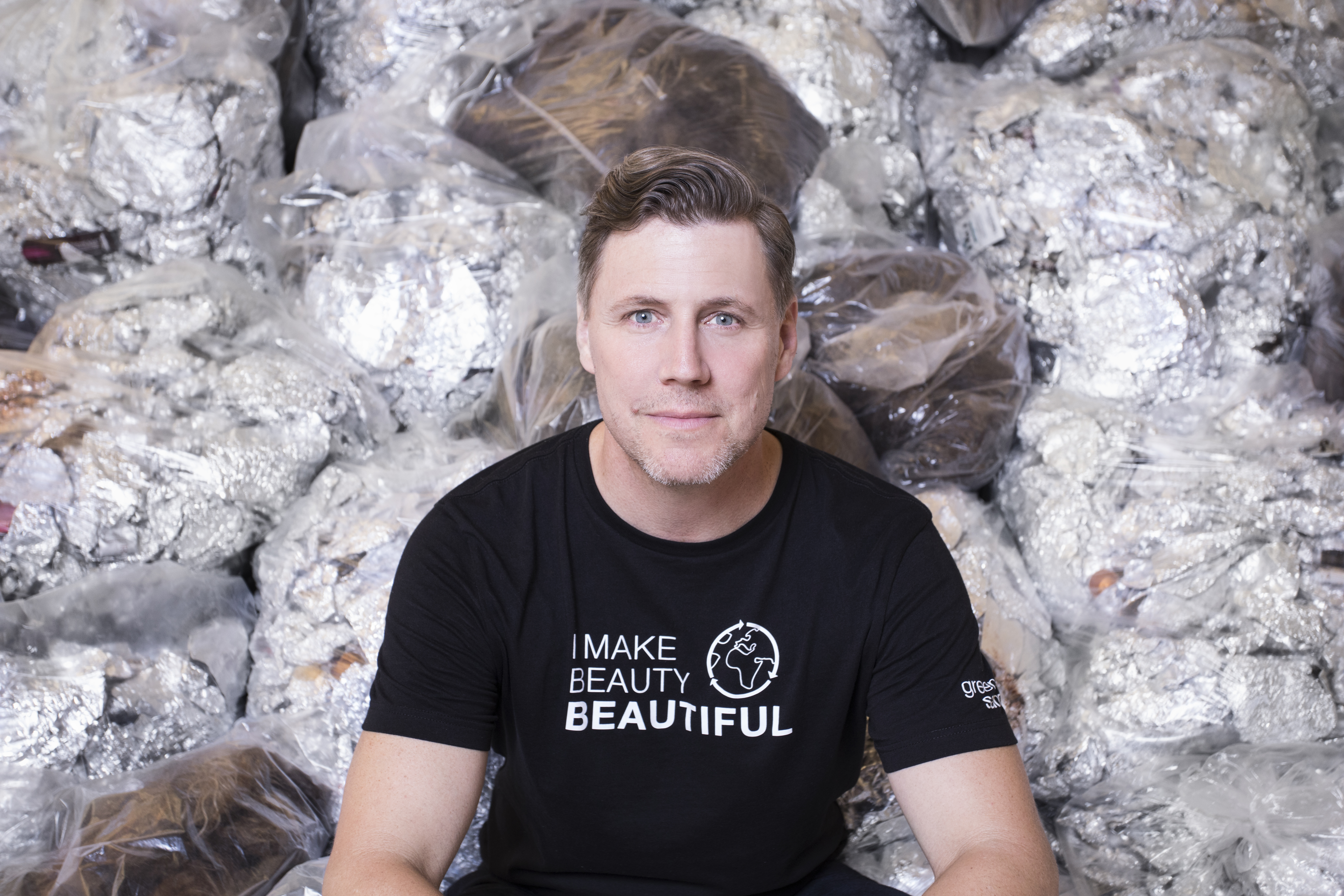 Closeup of Man in Black T-Shirt sitting in front of bags of recycled salon waste
