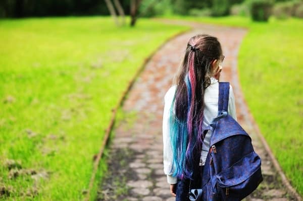 girl wearing purple backpack and blue and pink striped hair walking to school