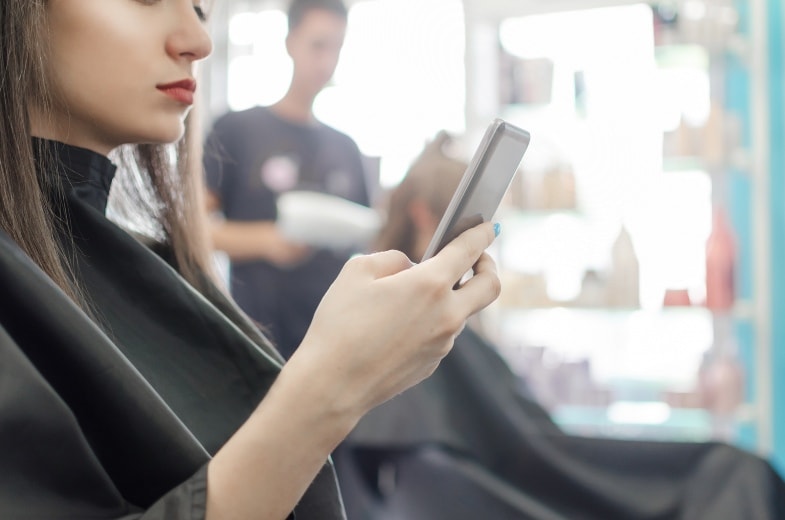 Woman sitting in salon chair checking her cell phone