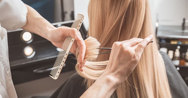 Hair stylist trimming blonde female hair