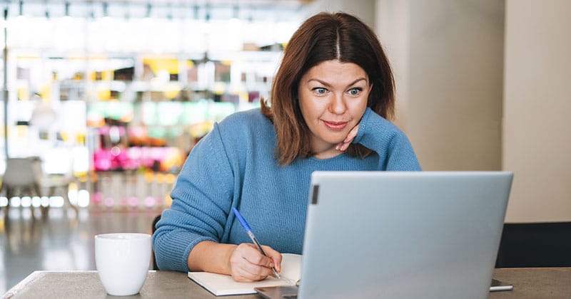 woman reading a laptop and taking notes