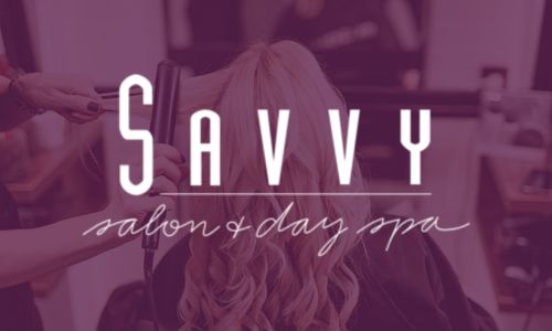 A person gets their hair styled with a curling iron in a salon. Overlaid text reads: "Savvy salon & day spa." The background is tinted with a soft purple hue.
