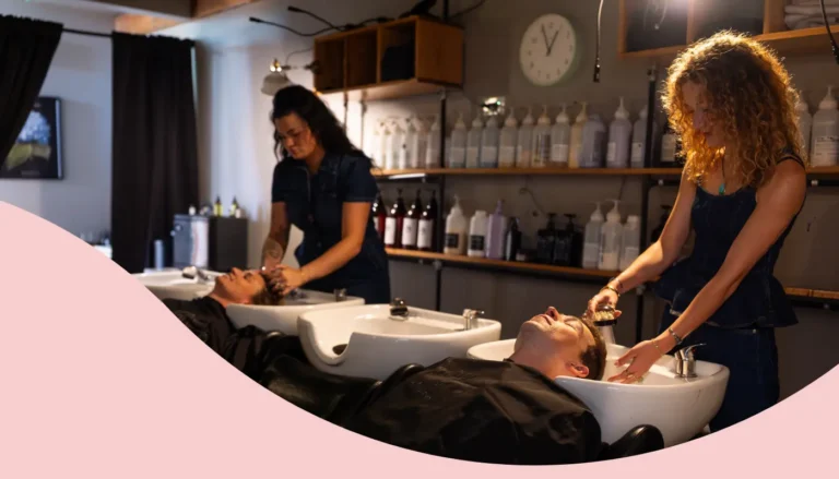 Two salon stylists washing their clients' hair at the wash bowl station