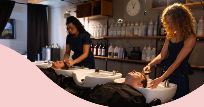 Two salon stylists washing their clients' hair at the wash bowl station