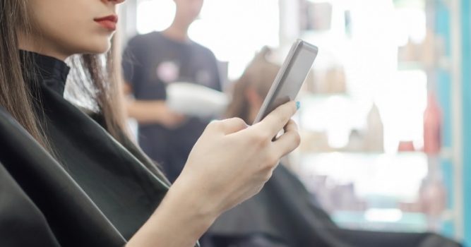Woman sitting in salon chair checking her cell phone