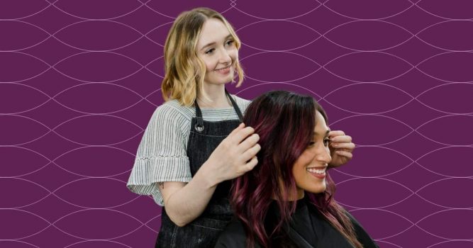 Hairstylist styles a client’s vibrant burgundy hair while both smile, set against a purple branded background with a subtle wave pattern. The image highlights personalized salon services, client care, and professional hairstyling expertise.