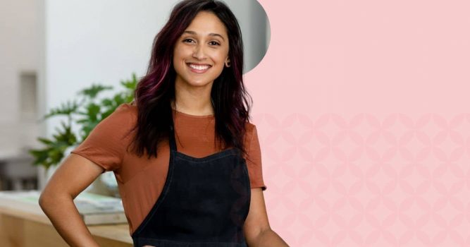 Smiling salon professional stands confidently in a modern salon wearing a black apron. The image features a soft pink branded background with subtle geometric patterns, highlighting salon business management, professionalism, and beauty industry expertise.